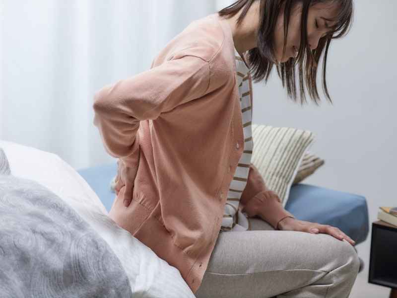 mujer sentada en la cama con dolor de espalda al despertar